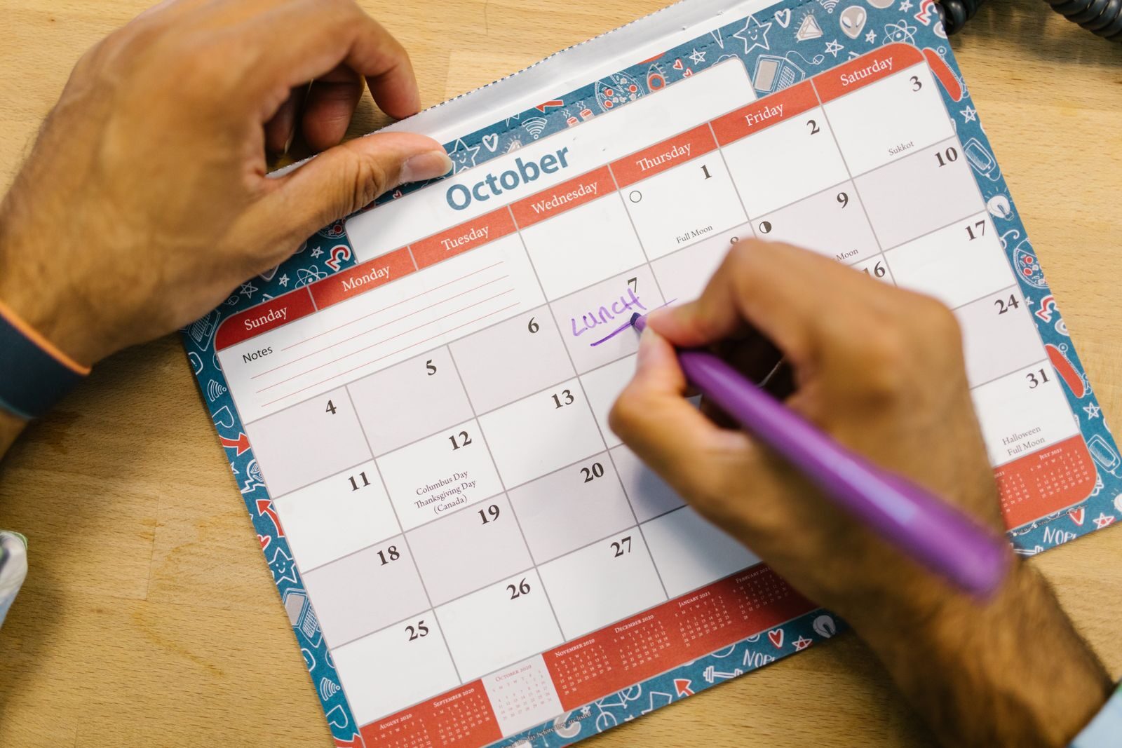 Mão anotando um lembrete em um calendário mensal com caneta, representando a troca semanal do adesivo anticoncepcional
