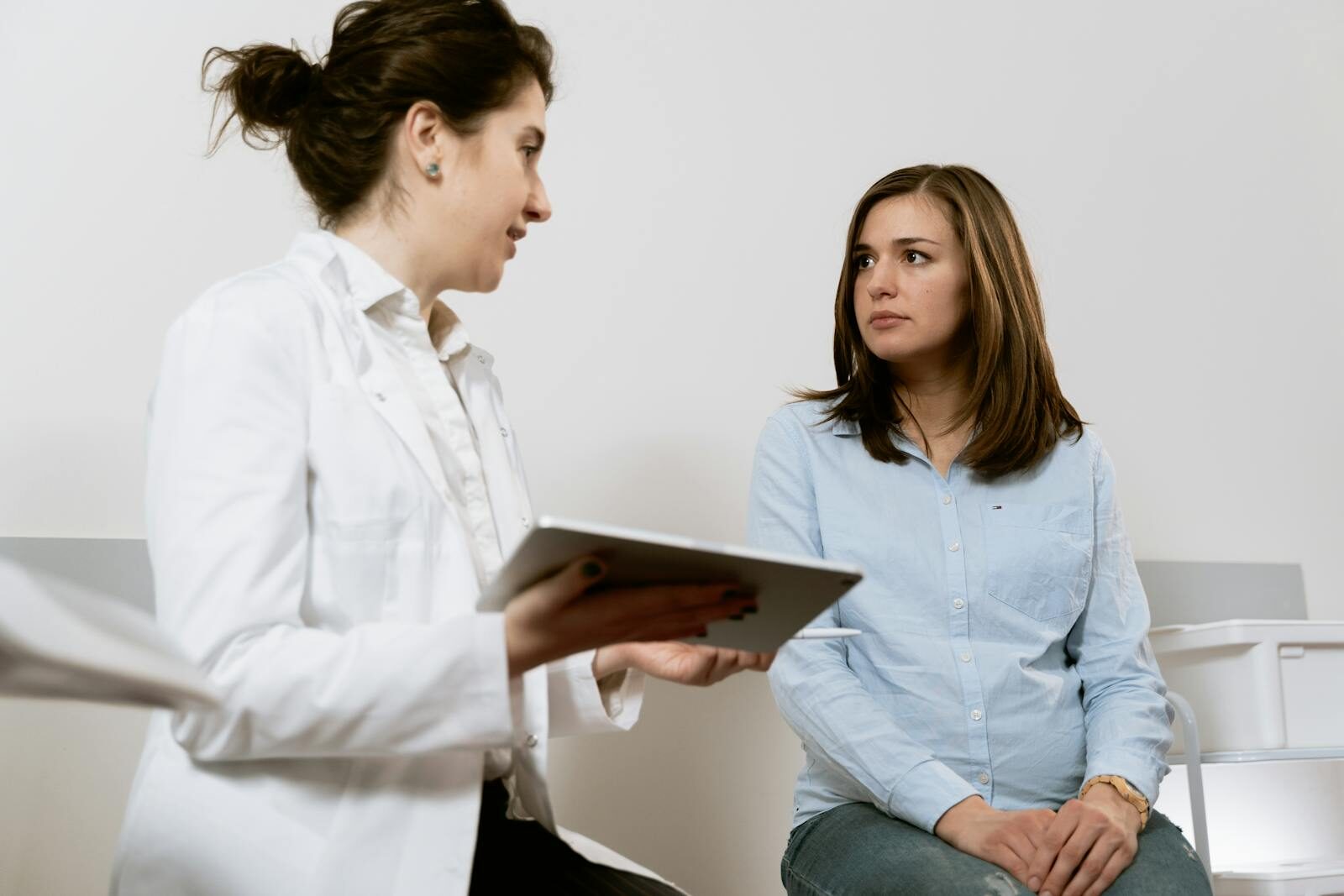 Médica de jaleco branco conversando com uma paciente durante consulta ginecológica em um consultório claro e acolhedor