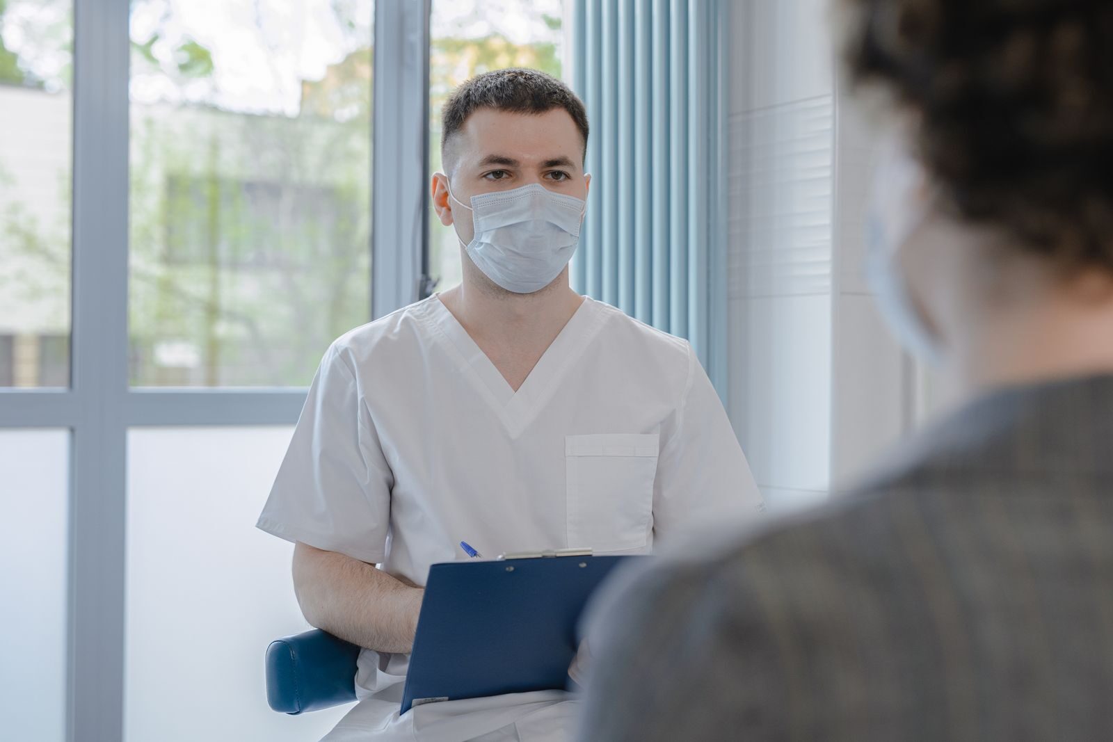 Profissional de saúde em jaleco conversa com uma paciente e faz anotações durante uma consulta em consultório claro e acolhedor