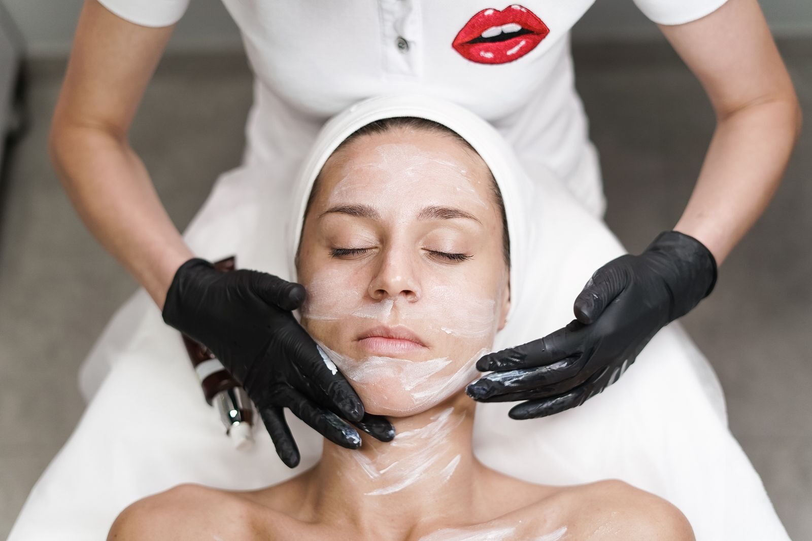 Mulher relaxada deitada recebendo tratamento estético de pele aplicado por uma profissional em um spa moderno e iluminado