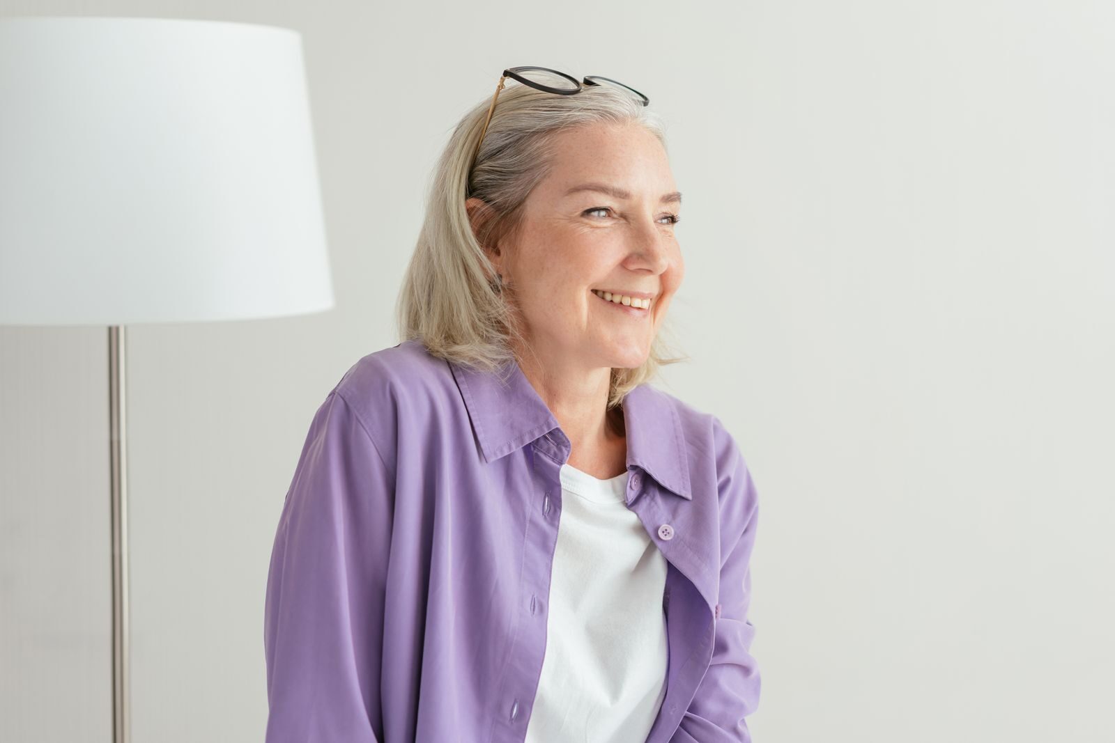 Mulher madura de cabelos grisalhos sorrindo de forma serena e confiante em um ambiente claro e acolhedor, representando o bem-estar feminino durante o climatério e a menopausa