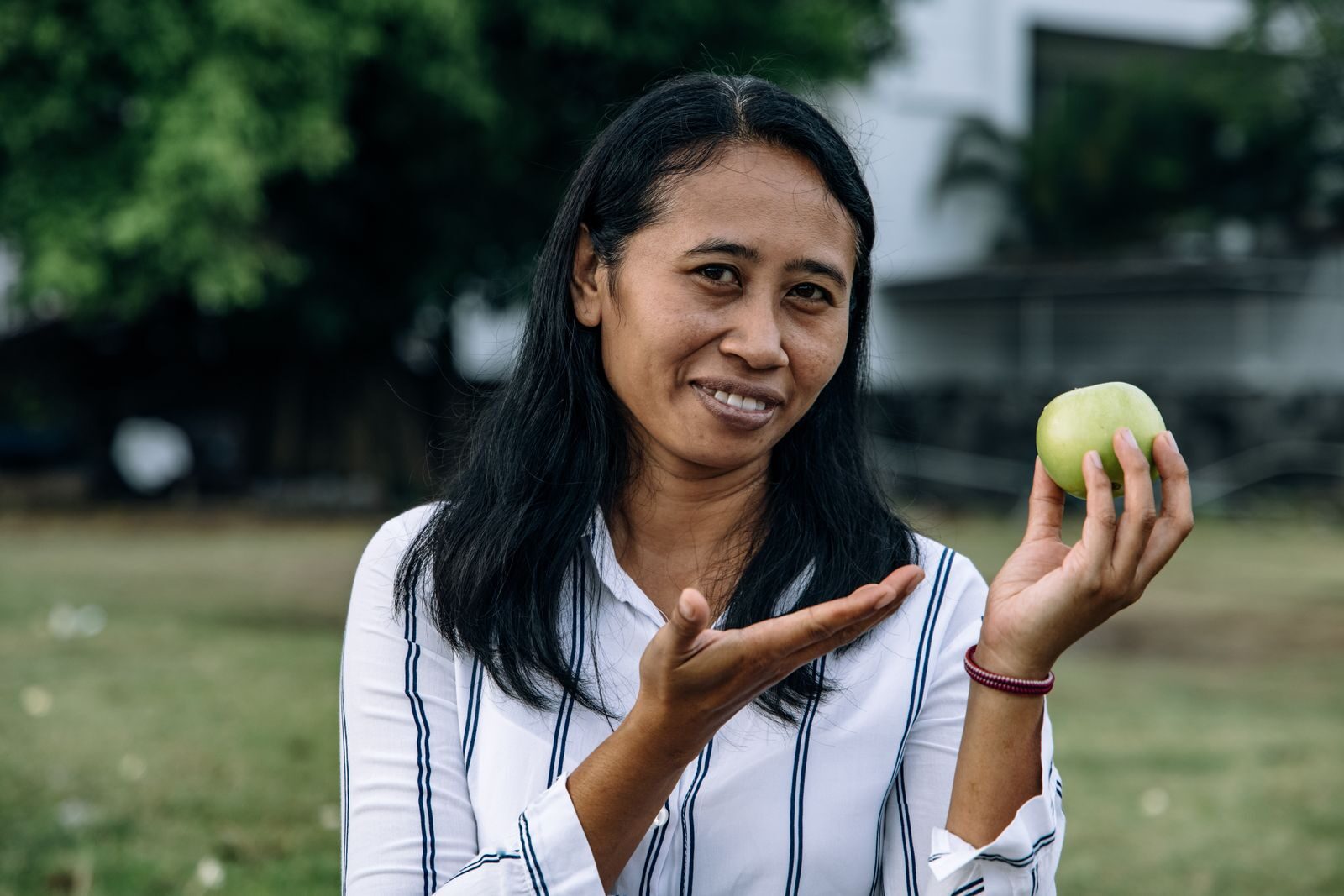 Mulher sorridente ao ar livre segurando uma maçã verde, transmitindo saúde, bem-estar e autocuidado feminino
