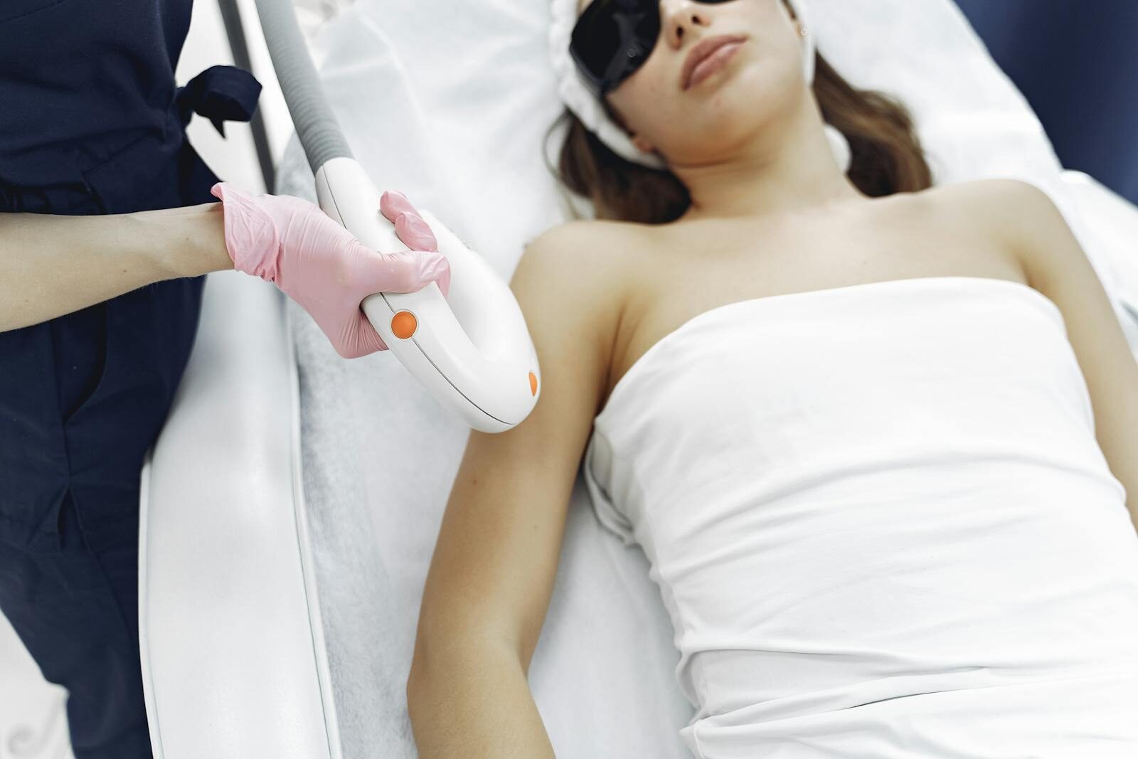 Profissional de estética realizando sessão de depilação a laser em uma cliente que usa óculos de proteção, em ambiente clínico claro e higienizado.