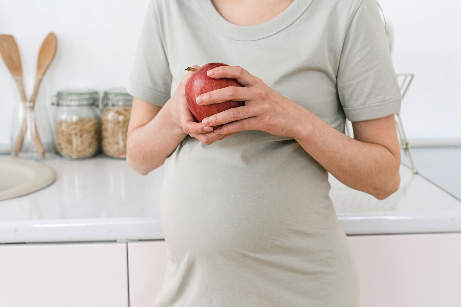 Gestante segurando uma maçã vermelha em uma cozinha clara, simbolizando alimentação saudável durante a gravidez