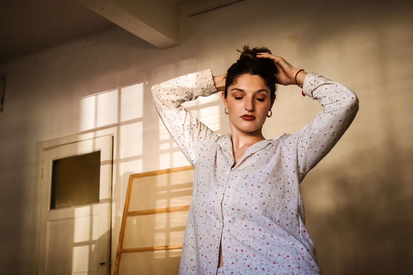 Mulher tranquila de olhos fechados em um quarto iluminado pela luz natural, transmitindo calma e bem-estar