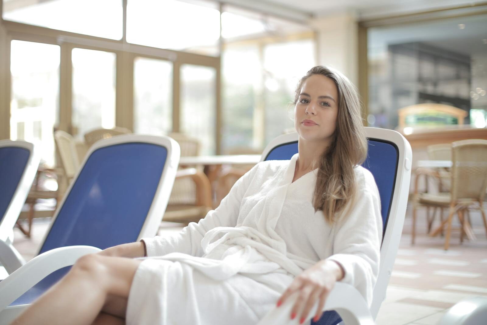 Mulher jovem sorridente e relaxada em um roupão branco descansando em uma poltrona de spa, em um ambiente clean de bem-estar e cuidados pessoais