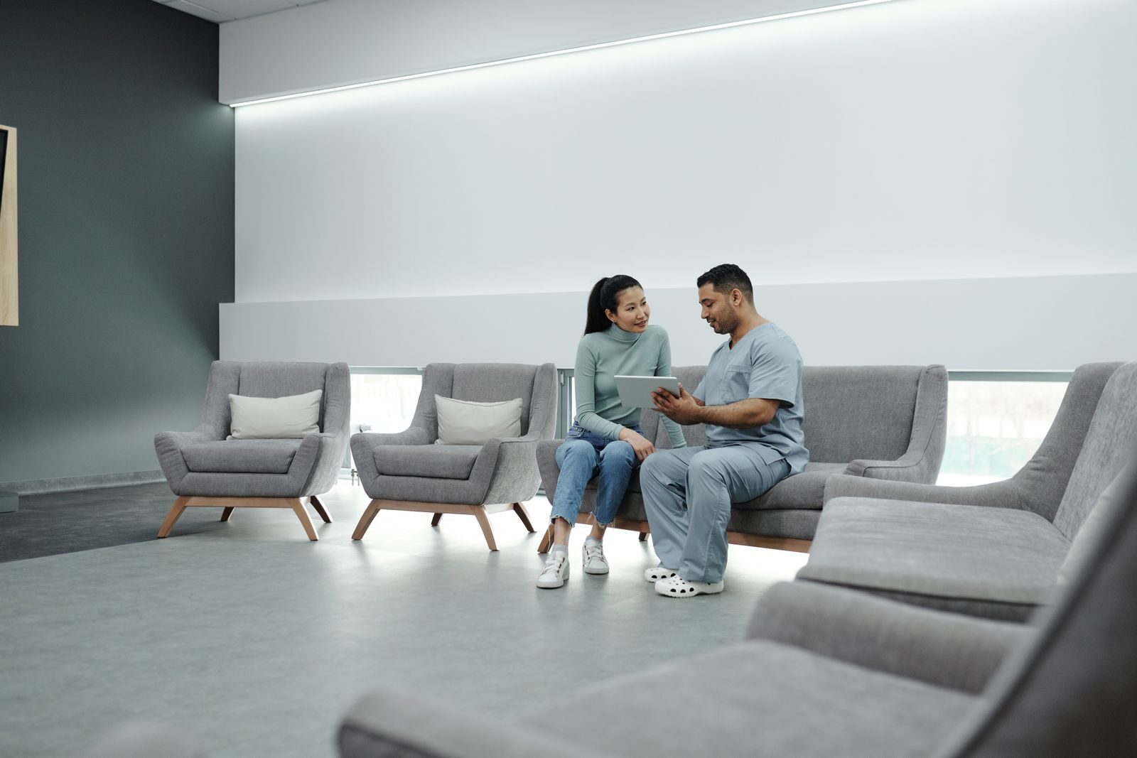 Médica em jaleco conversa com uma paciente durante consulta em um consultório moderno e bem iluminado, segurando um tablet