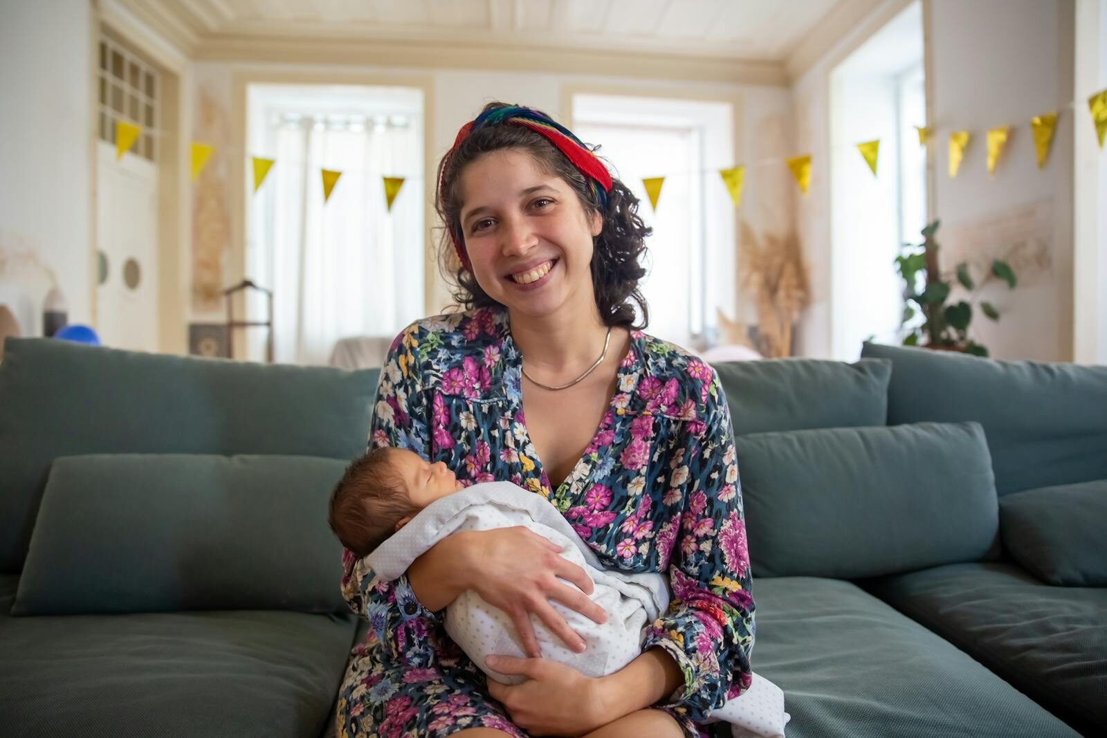Mãe sorridente segurando seu bebê recém-nascido no colo em uma sala iluminada e acolhedora, representando o período pós-parto e a amamentação