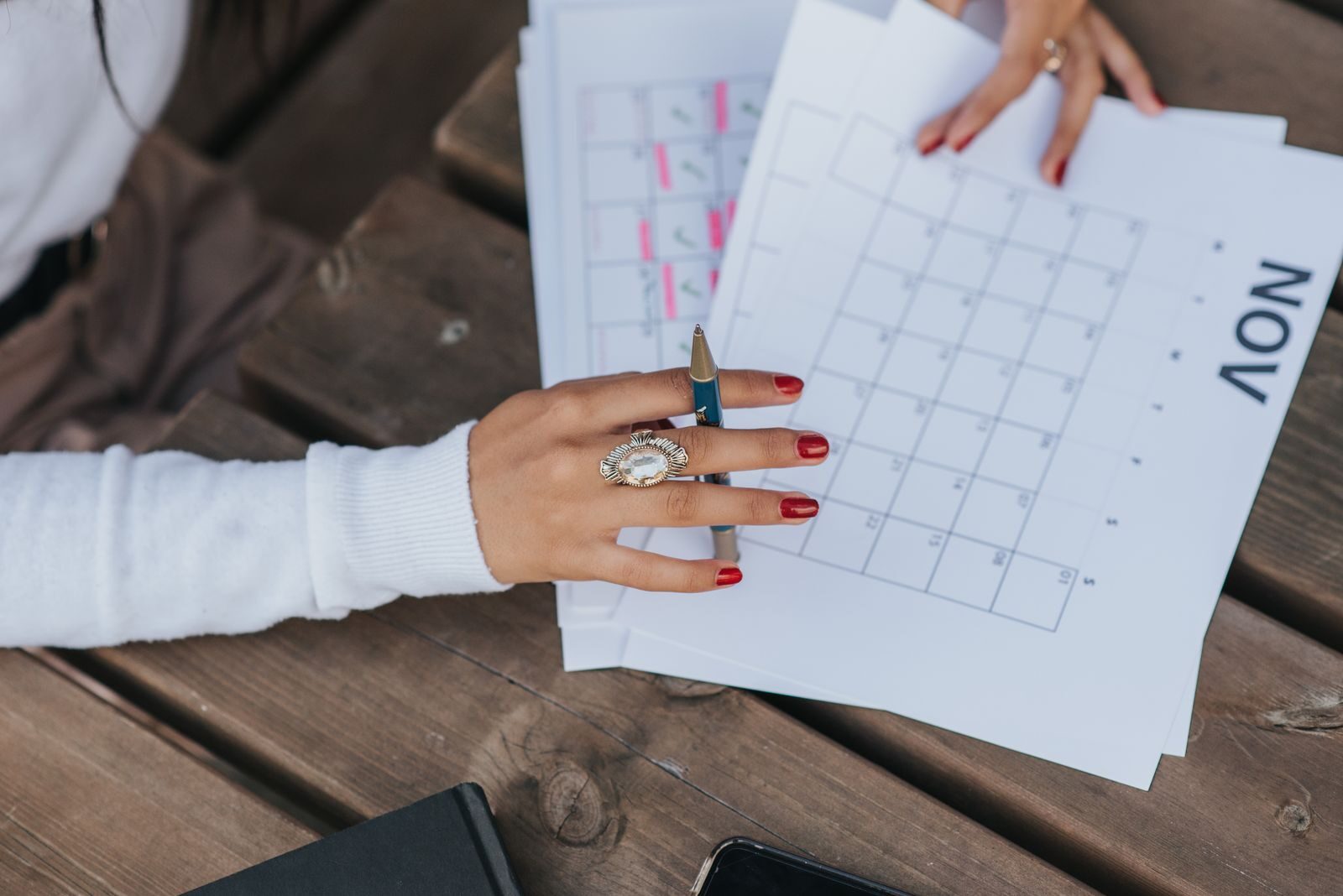 Mulher anotando datas em um calendário de papel sobre uma mesa de madeira, simbolizando o planejamento do tempo de proteção do implante contraceptivo