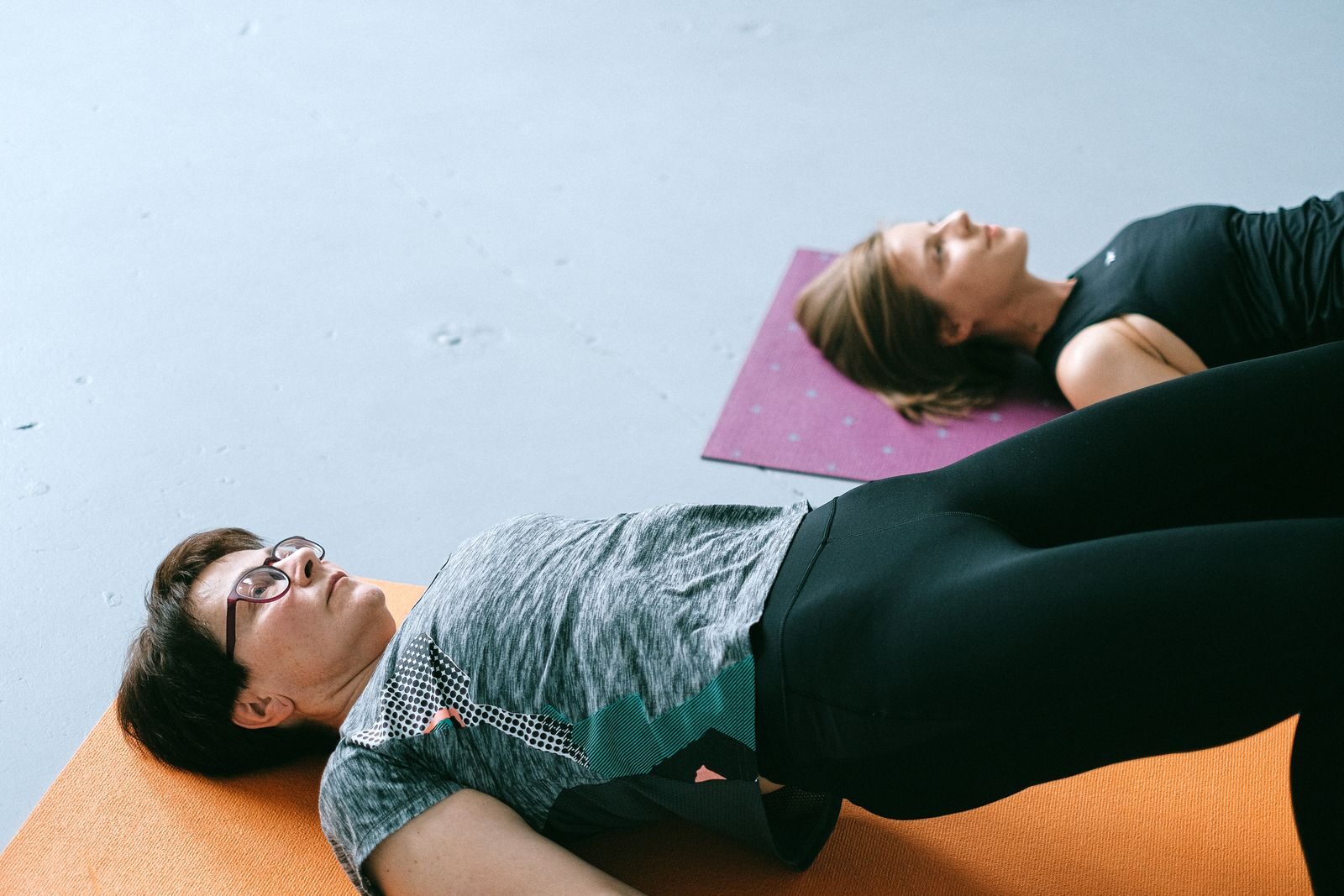 Duas mulheres deitadas em colchonetes fazendo exercicios de fortalecimento do assoalho pelvico em um estudio claro, representando a fisioterapia pelvica no tratamento da incontinencia urinaria feminina