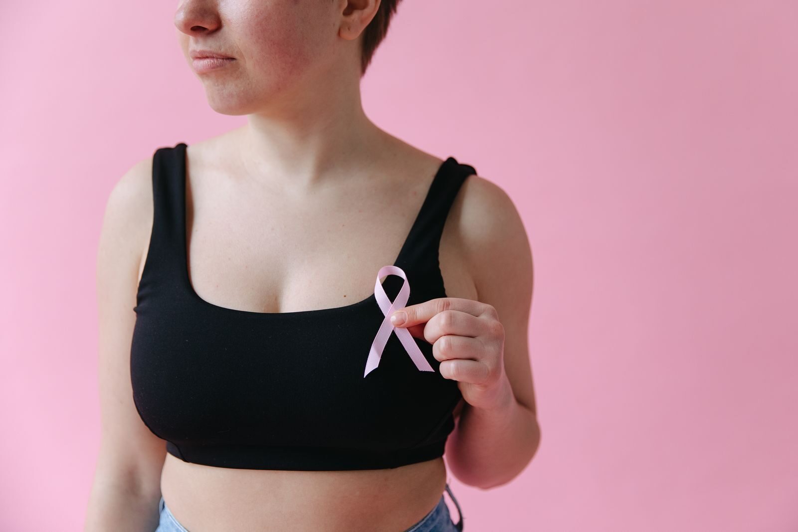 Mãos de uma mulher segurando um laço rosa, símbolo da conscientização e prevenção do câncer de mama