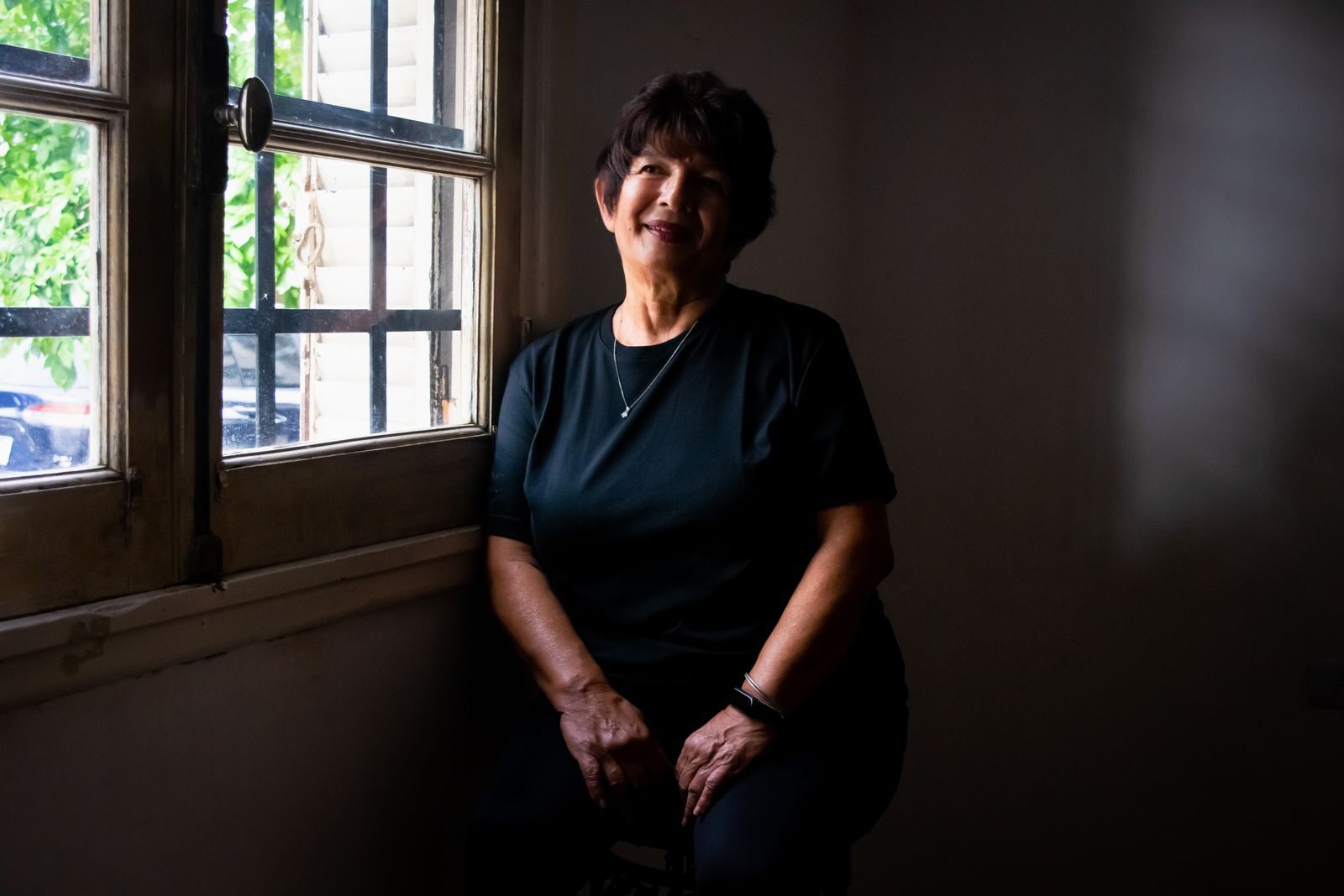 Mulher madura sentada serenamente perto de uma janela, iluminada por luz natural suave, em ambiente acolhedor