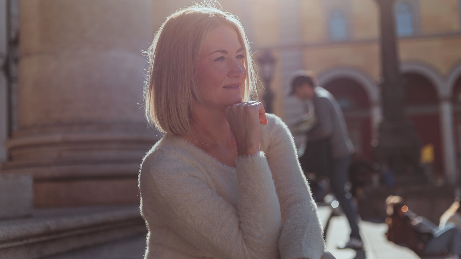 Mulher de meia-idade sorrindo serenamente ao ar livre, iluminada pela luz dourada do sol, transmitindo bem-estar e tranquilidade