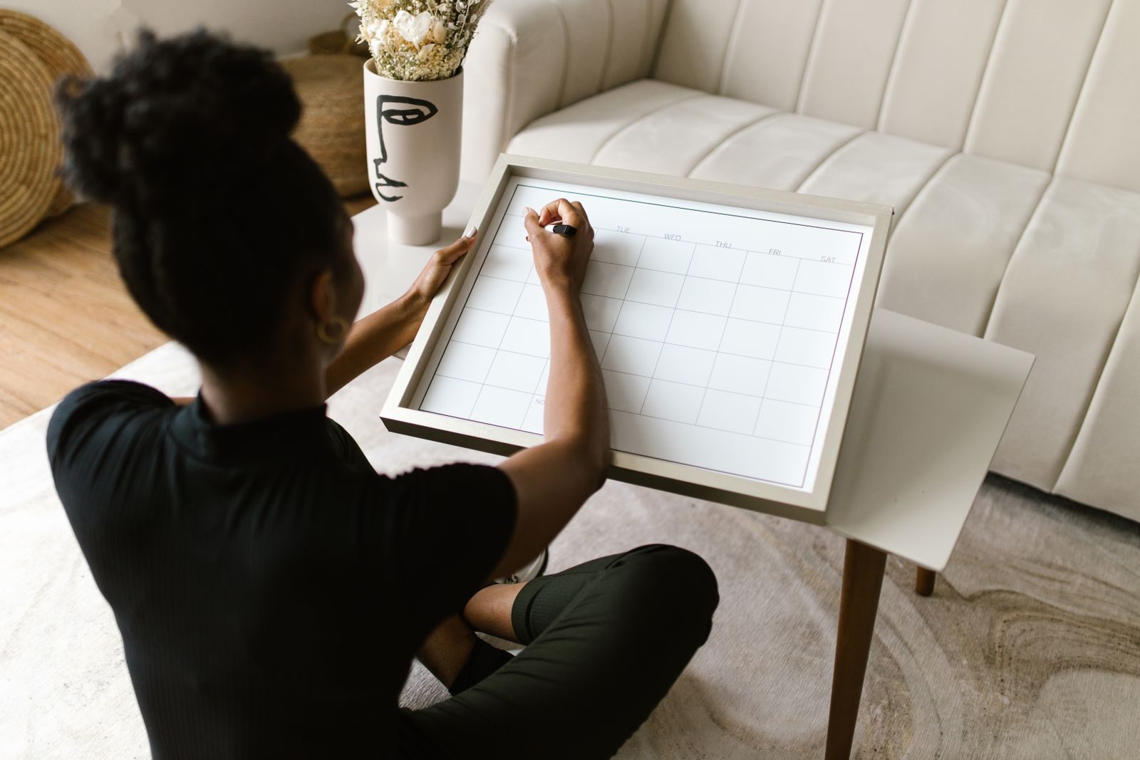Mulher sentada no chão de casa anotando datas em um calendário sobre uma mesinha, representando o acompanhamento do ciclo menstrual