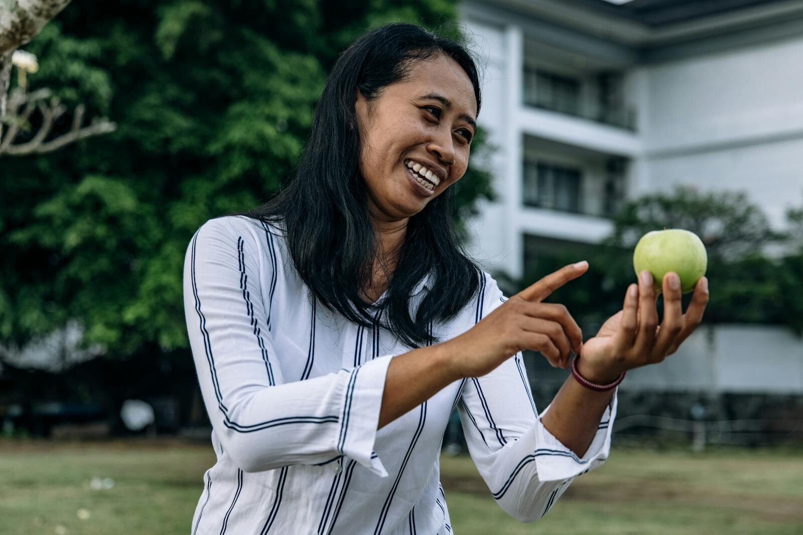 Mulher sorridente ao ar livre segurando uma maçã verde, representando bem-estar e estilo de vida saudável