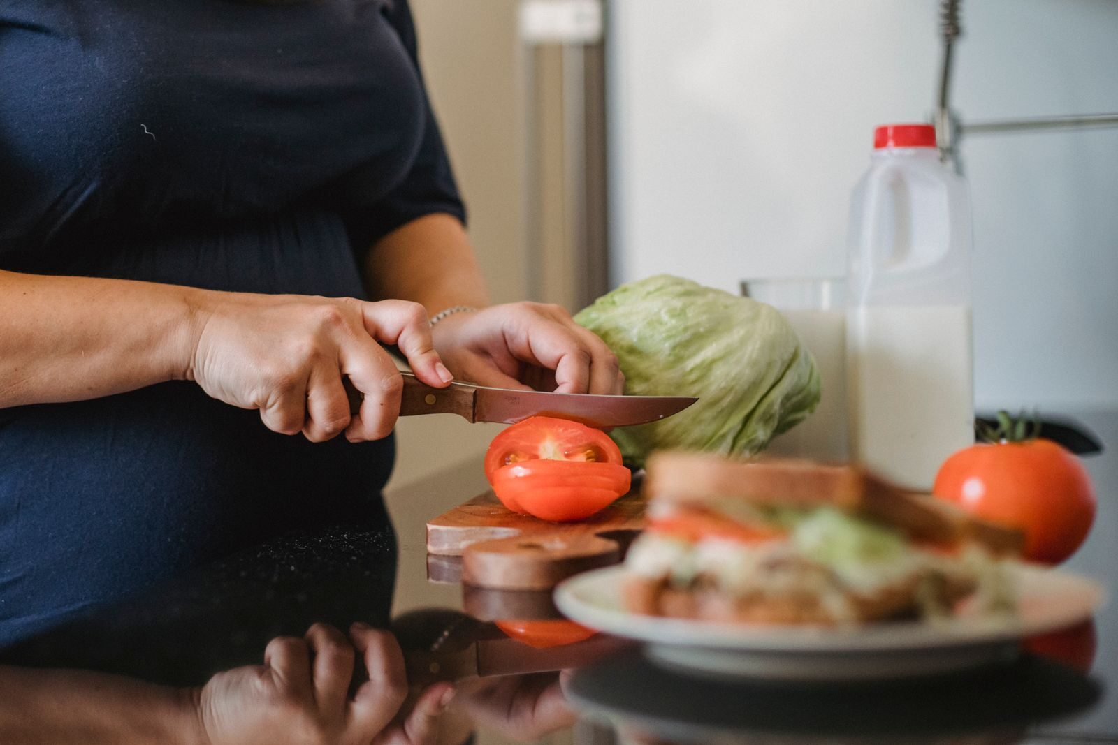 Mulher preparando refeição saudável, cortando tomates frescos sobre uma tábua de madeira em uma cozinha iluminada, representando alimentação e estilo de vida no manejo do ovário policístico