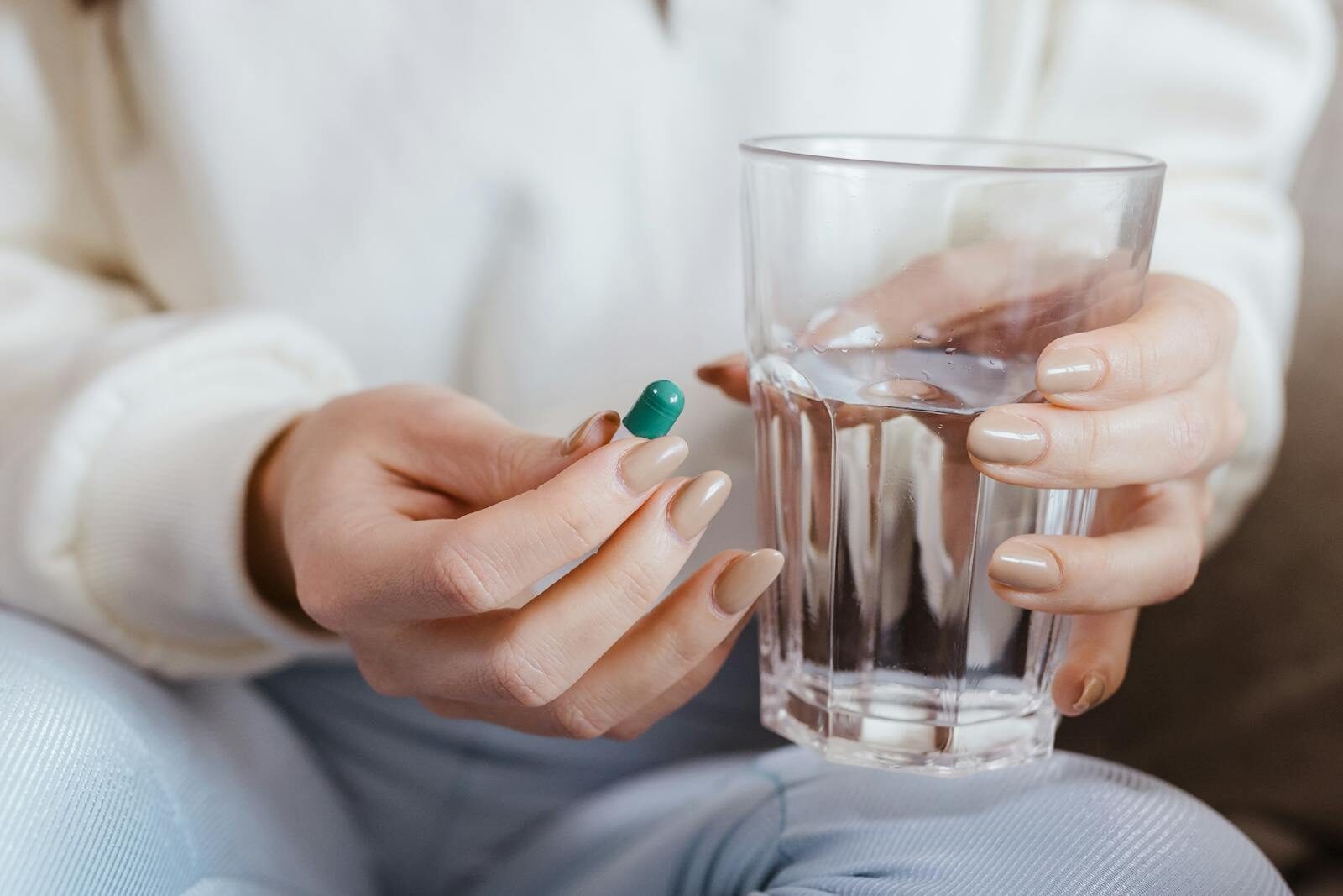 Mãos de uma mulher segurando um comprimido em uma das mãos e um copo de água na outra, prestes a tomar o medicamento