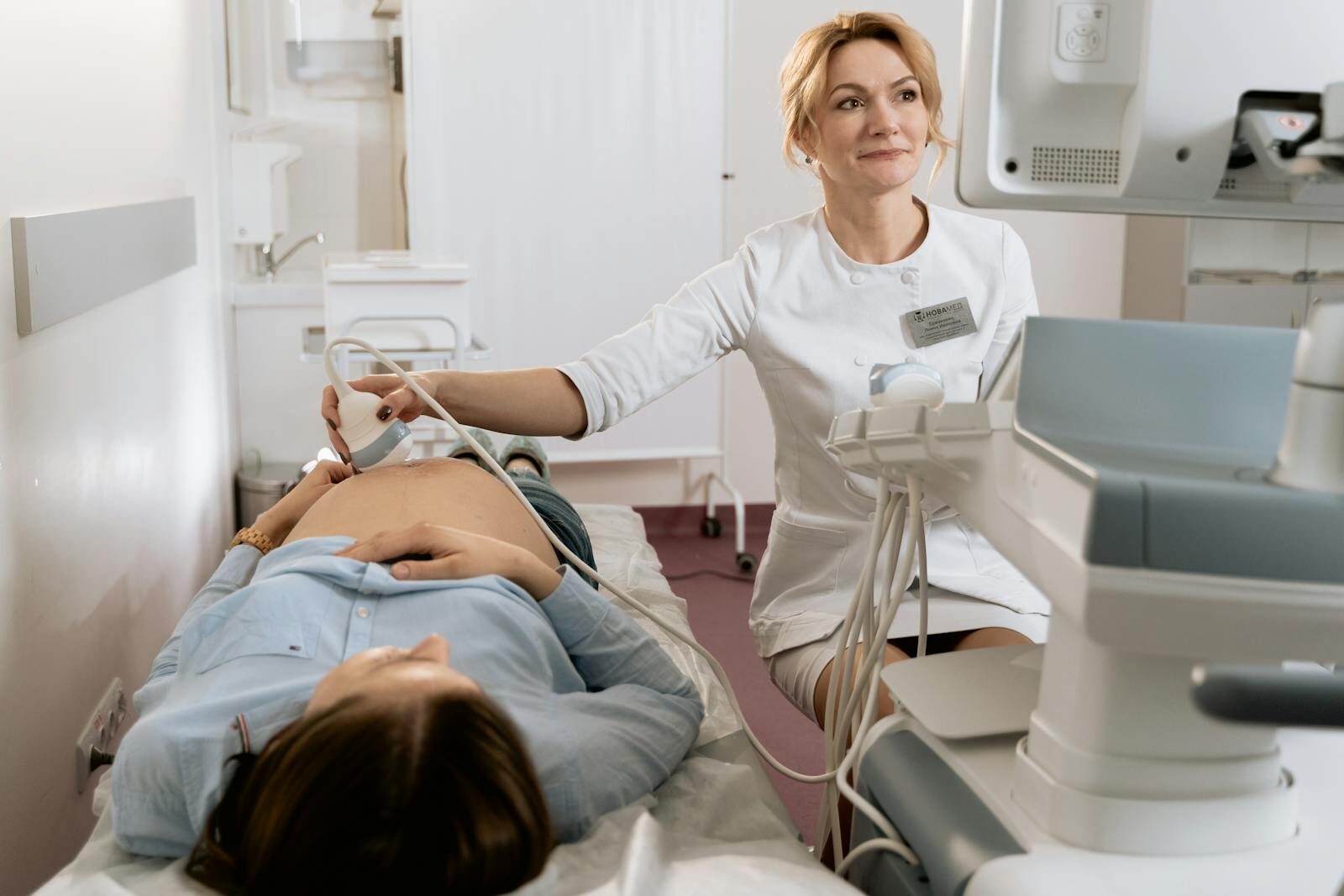 Médica obstetra realizando exame de ultrassom em uma gestante deitada em uma maca de consultório, durante consulta de pré-natal em clínica de saúde da mulher