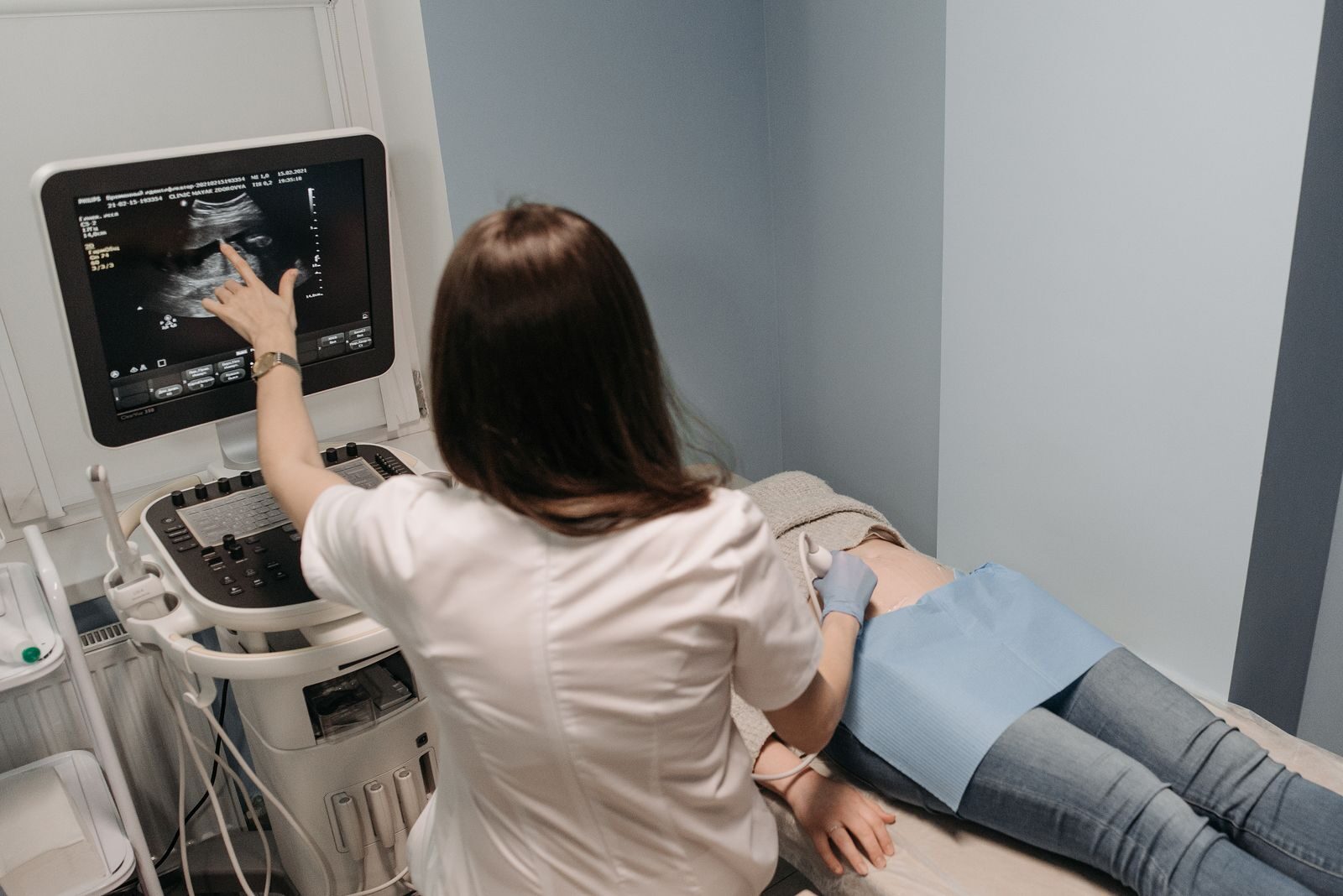 Médica realizando exame de ultrassom em paciente gestante e apontando para a tela do equipamento em uma clínica